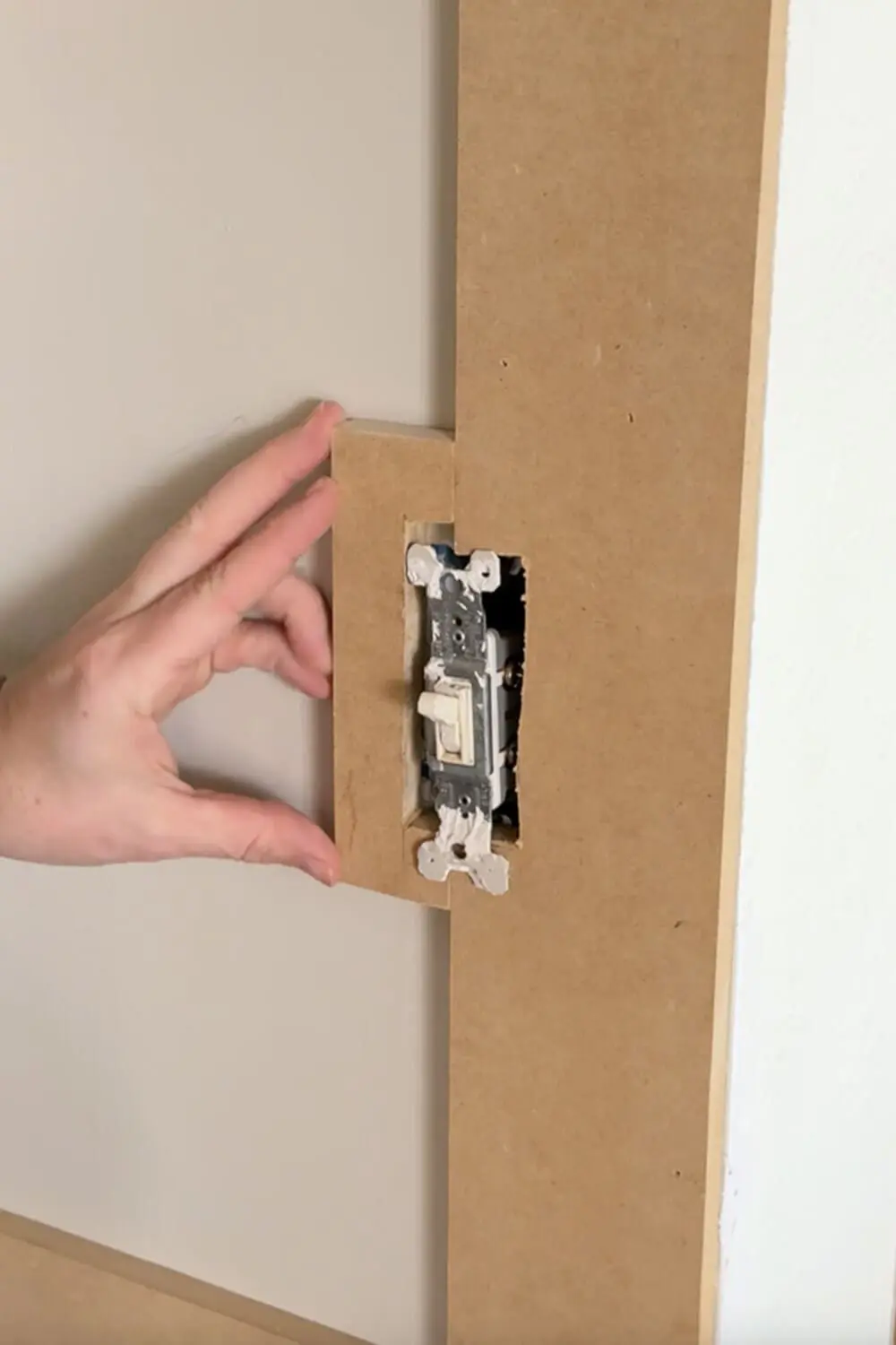 Notching a DIY box molding wall trim board to fit around a light switch, showing how to work around electrical boxes during wall panel installation.
