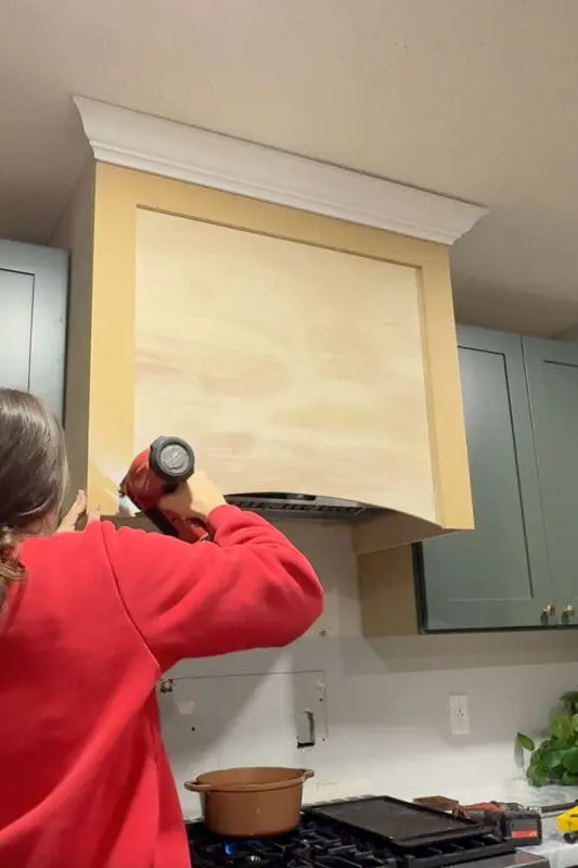 Attaching face-frame trim to a DIY wood range hood cover with a brad nailer, creating a clean framed front around the arched opening.