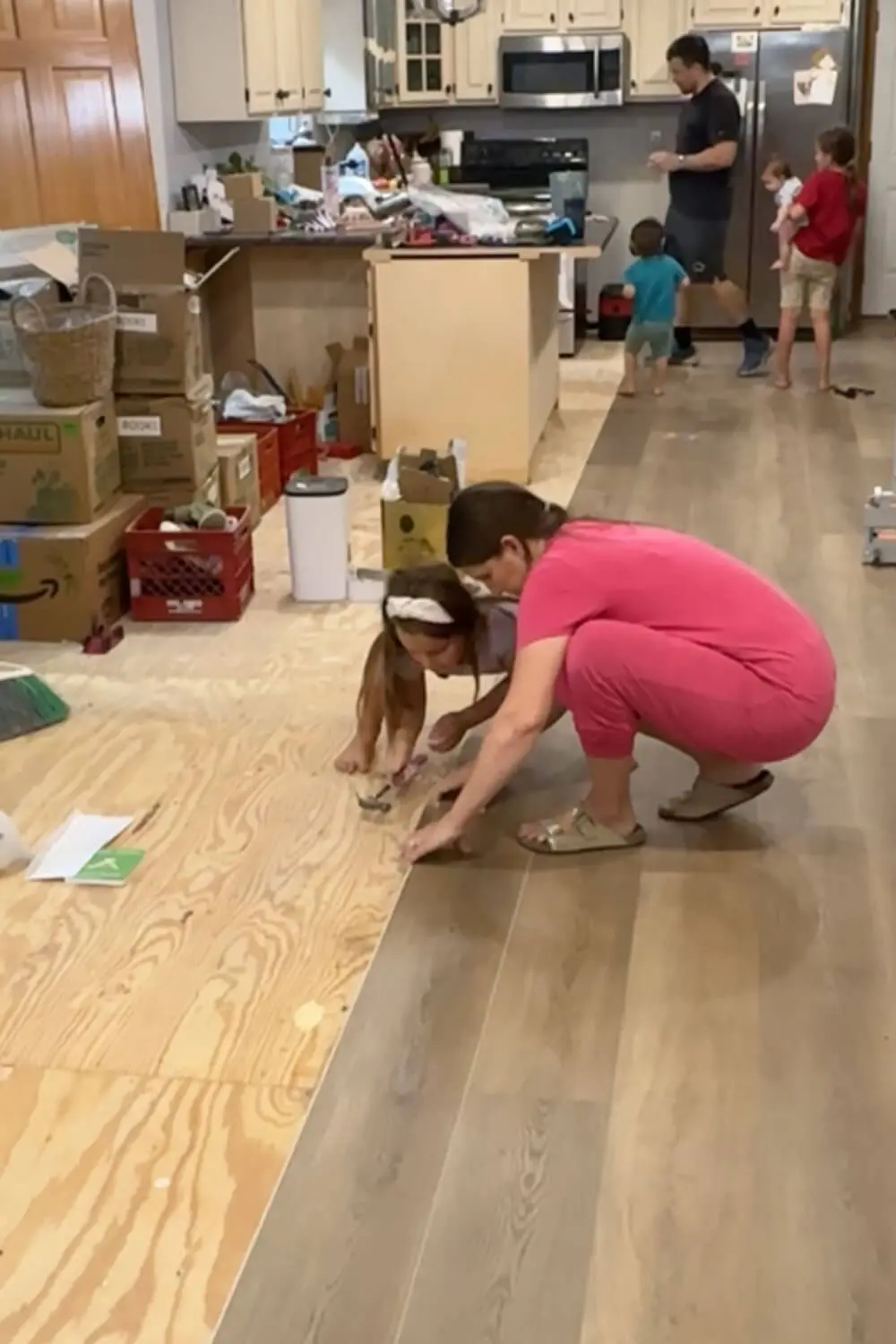 Installing wide plank flooring in the kitchen over the plywood subfloor, with our family helping line up and tap the planks into place during the renovation.