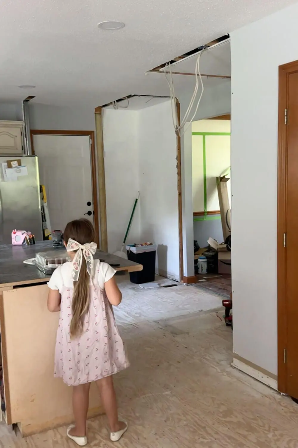 Same kitchen view after demo with the closet and pantry removed, drywall and ceiling opened up with exposed wiring, and the space opened up around the temporary island during renovation.