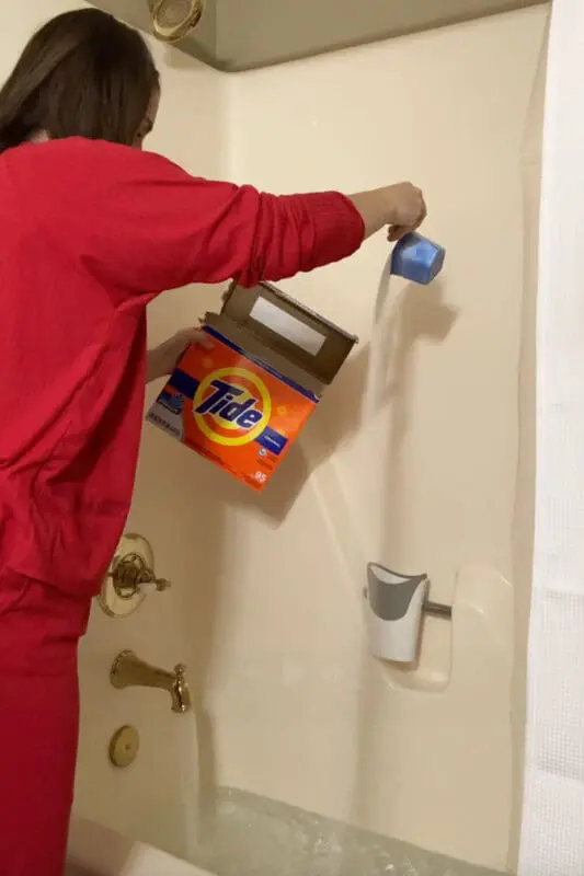 Pouring powdered Tide detergent into a bathtub of hot water to start laundry stripping and remove gross buildup and odors from clothes.