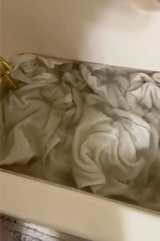 White towels soaking in a bathtub during laundry stripping, with cloudy water showing detergent buildup and residue being pulled out of the fabric.