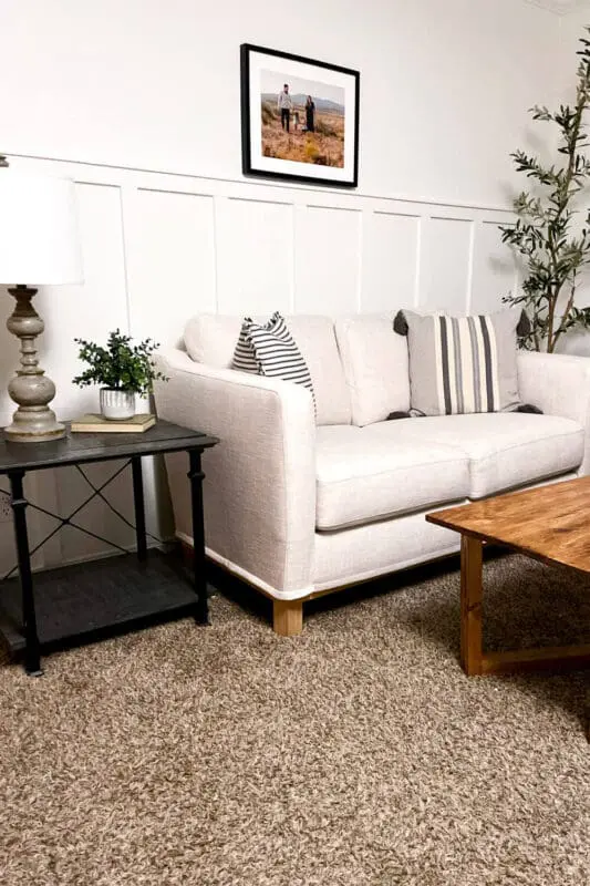 Finished living room wall molding accent wall painted white behind a light sofa, showing vertical panel trim with cozy neutral styling.