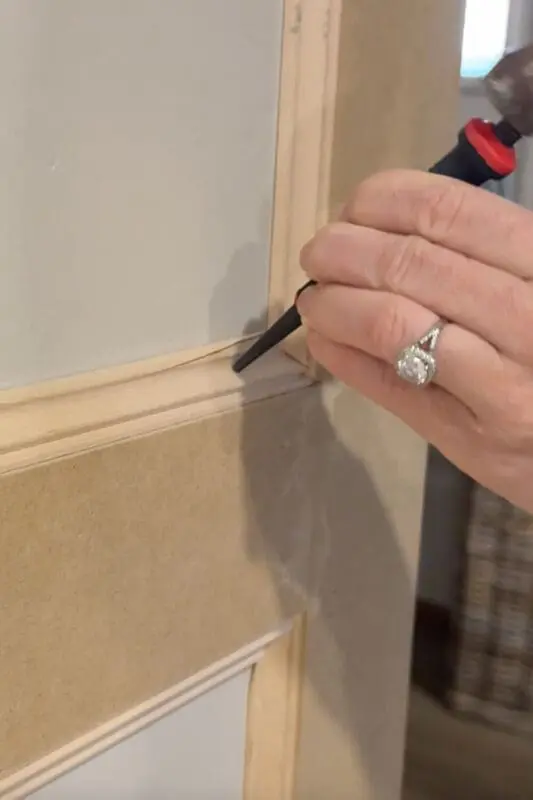 Using a nail punch and hammer to sink a brad nail below the surface of box molding wall trim so it can be filled and painted smooth.