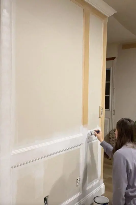 Priming DIY box molding wall trim with a paintbrush, covering the raw MDF so the wall panels and trim are ready for paint.