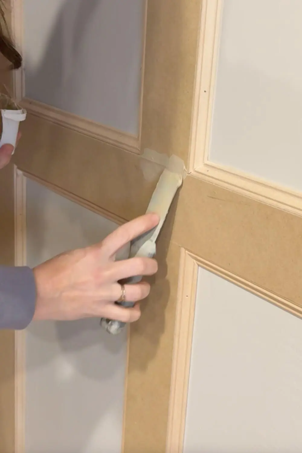 Applying primer over DIY box molding wall trim seams and nail holes with a brush to prep the MDF and trim joints for a smooth painted finish.