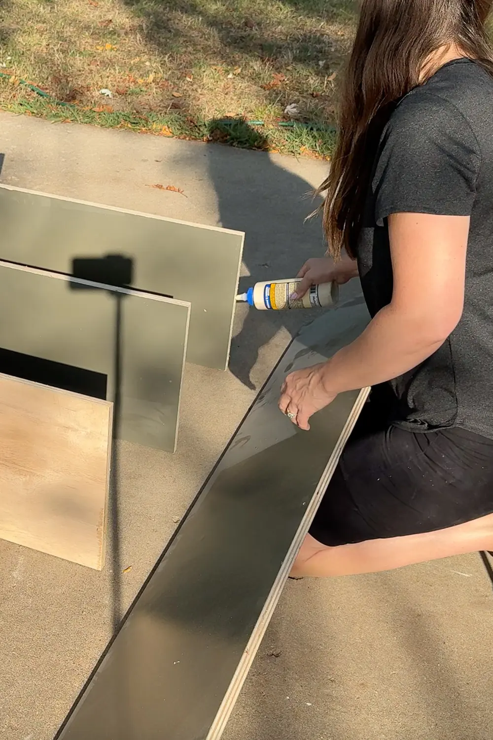 Applying wood glue to a long bookshelf side panel while building DIY plywood bookshelves for a home library.