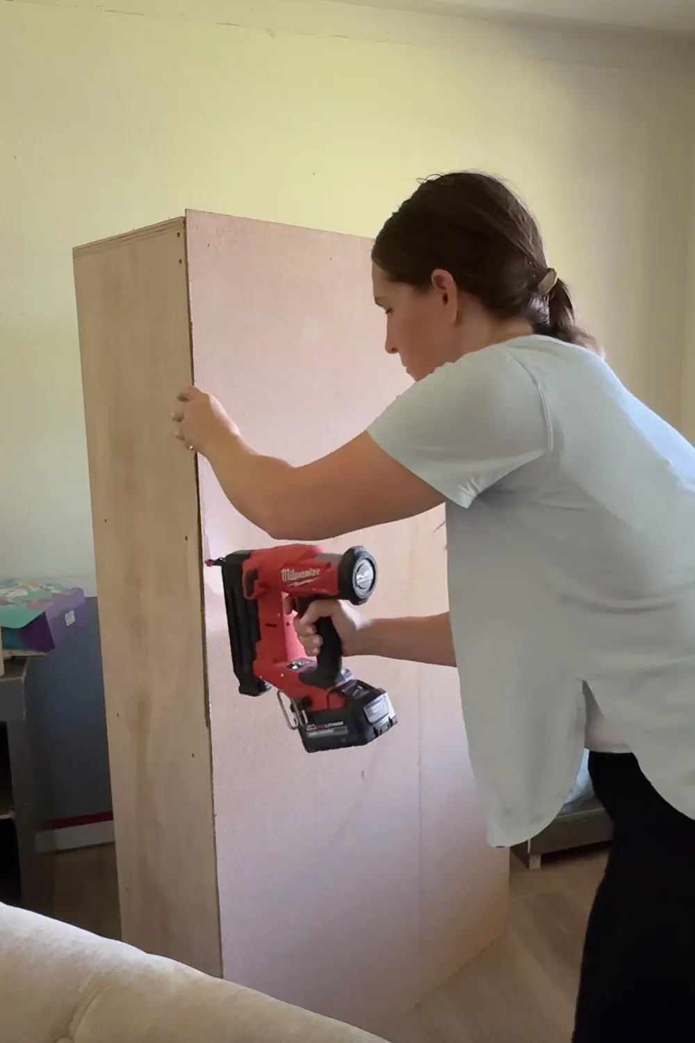Attaching the backing panel to the DIY bookshelf with a brad nailer to finish the home library shelving unit.