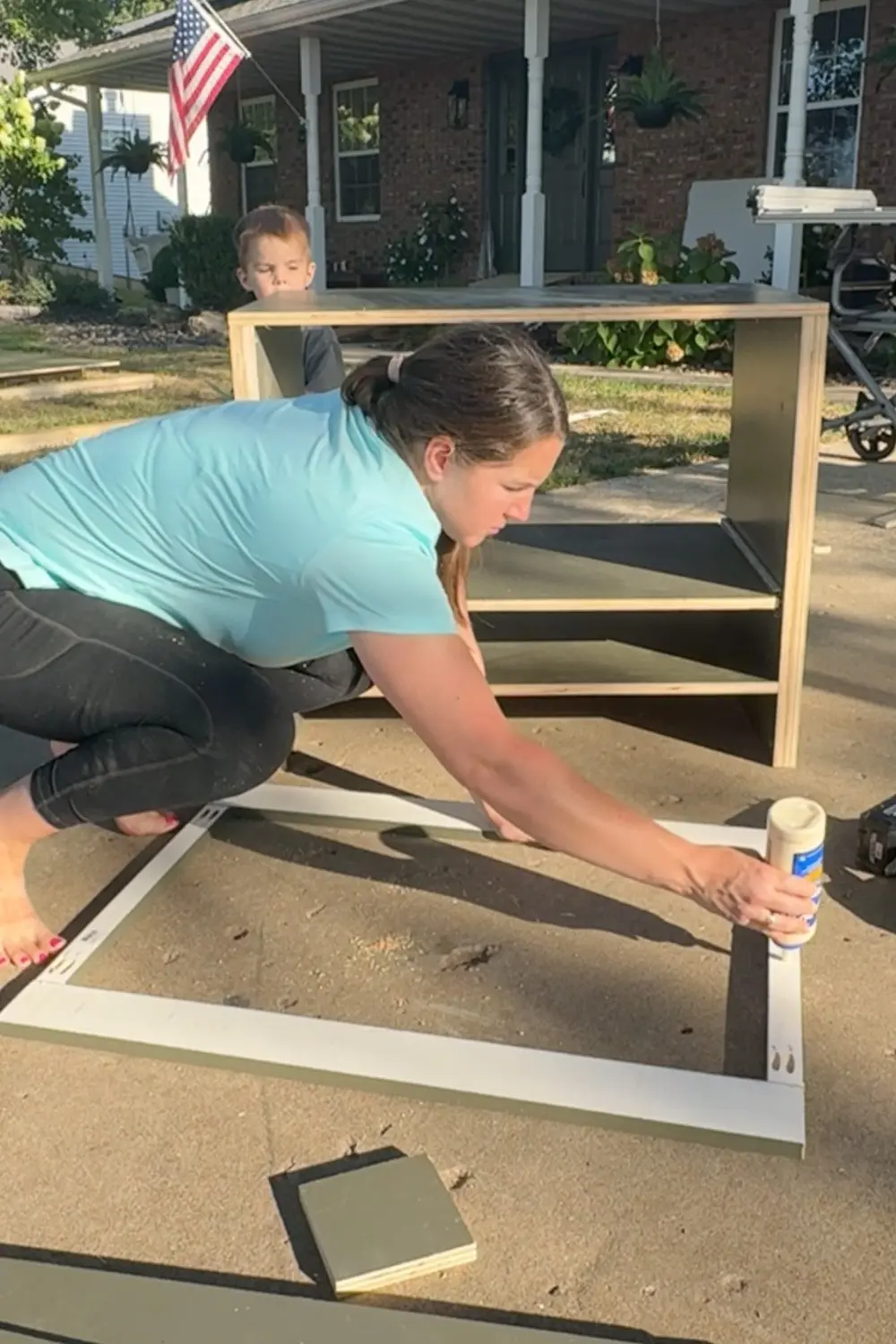 Applying wood glue to a DIY cabinet face frame on a driveway before attaching it to the front of a base cabinet.
