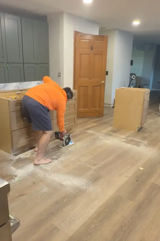 DIY kitchen island installation prep, cutting out the floating floor with a circular saw so the island cabinets sit directly on the subfloor instead of on top of the flooring.