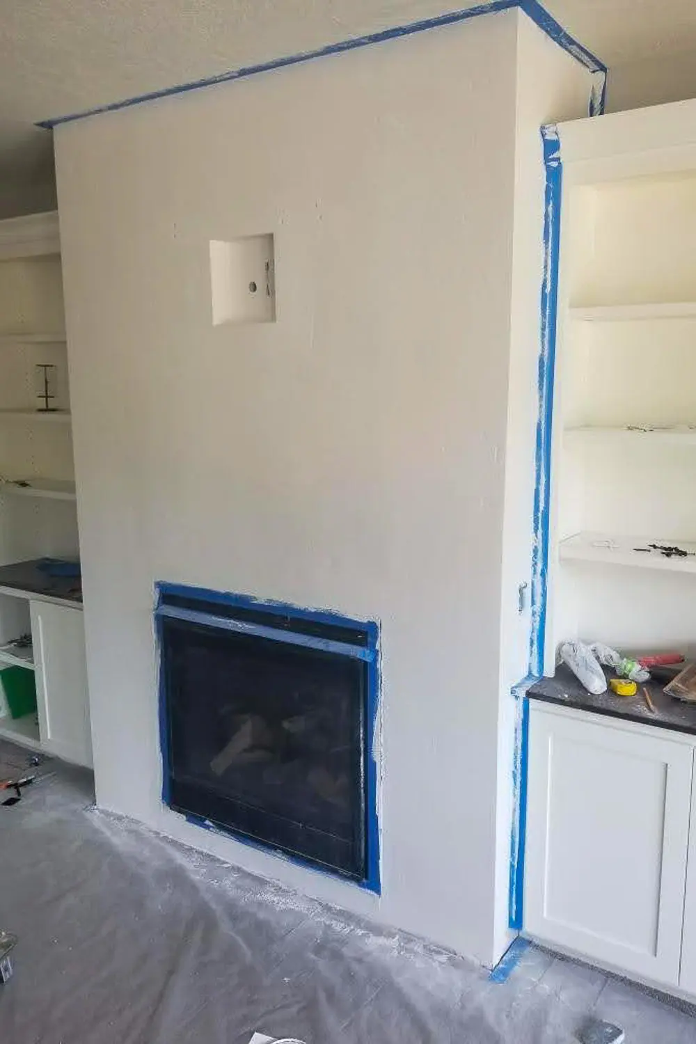Fireplace wall primed white and taped off with blue painters tape ready for plaster application, recessed media box visible above fireplace
