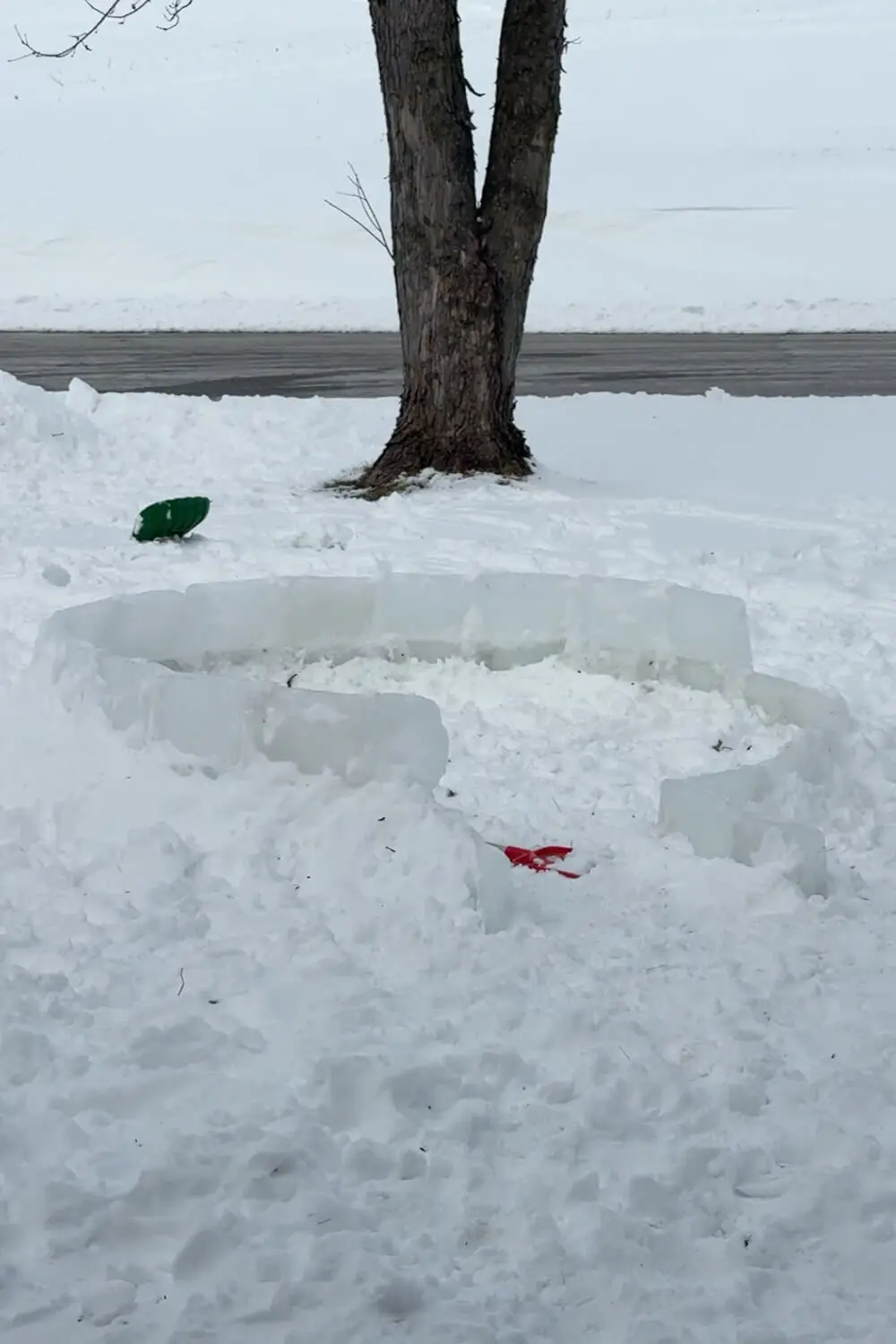 First rows of clear ice blocks stacked in a circle to start the base of a backyard igloo, showing the lower levels before building the dome for a how to build an igloo tutorial