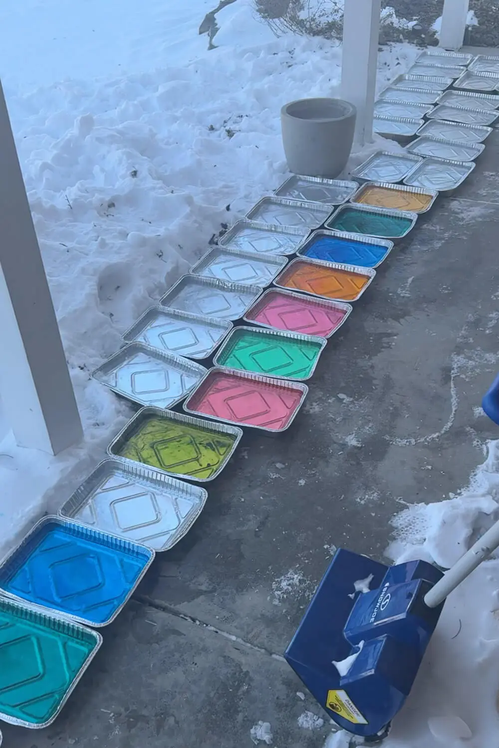 Aluminum pans lined up outside with water freezing into ice blocks, including colorful dyed blocks used for a how to build an igloo backyard project