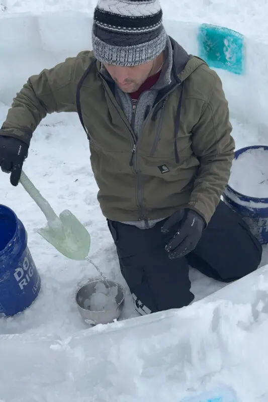 Using a small shovel to stir snow and water into slush for sealing ice blocks, showing how to make an awesome snow fort with homemade slush mortar and ice blocks