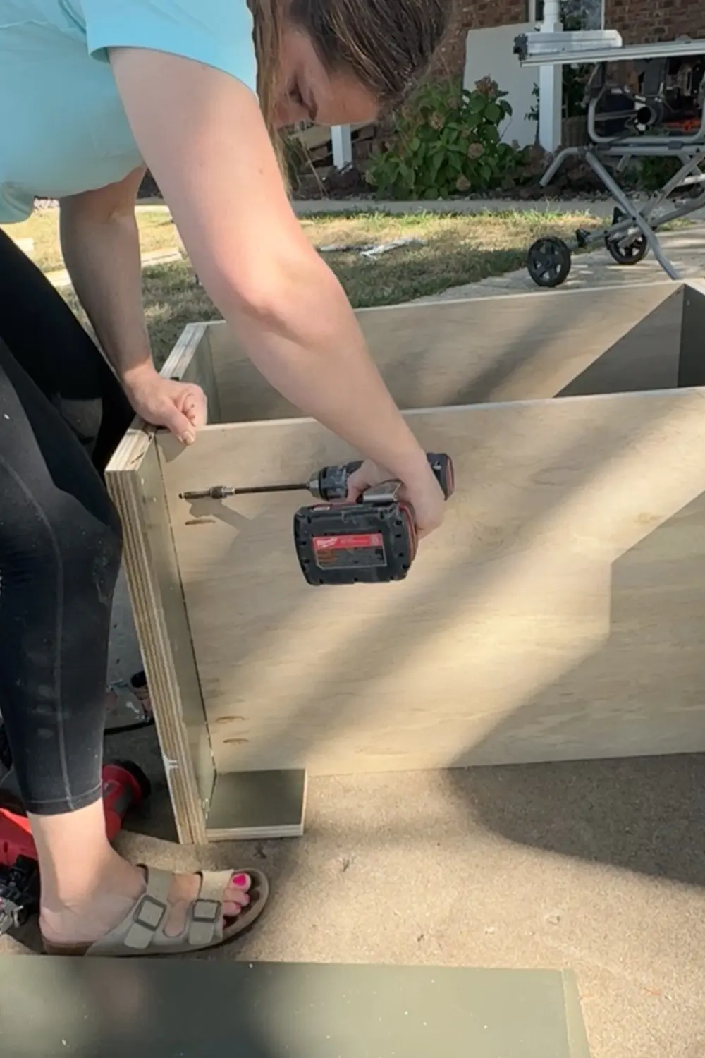 Drilling pocket hole screws to attach the plywood cabinet side to the bottom panel while building the base cabinets for our DIY built-in bookshelves and home library.