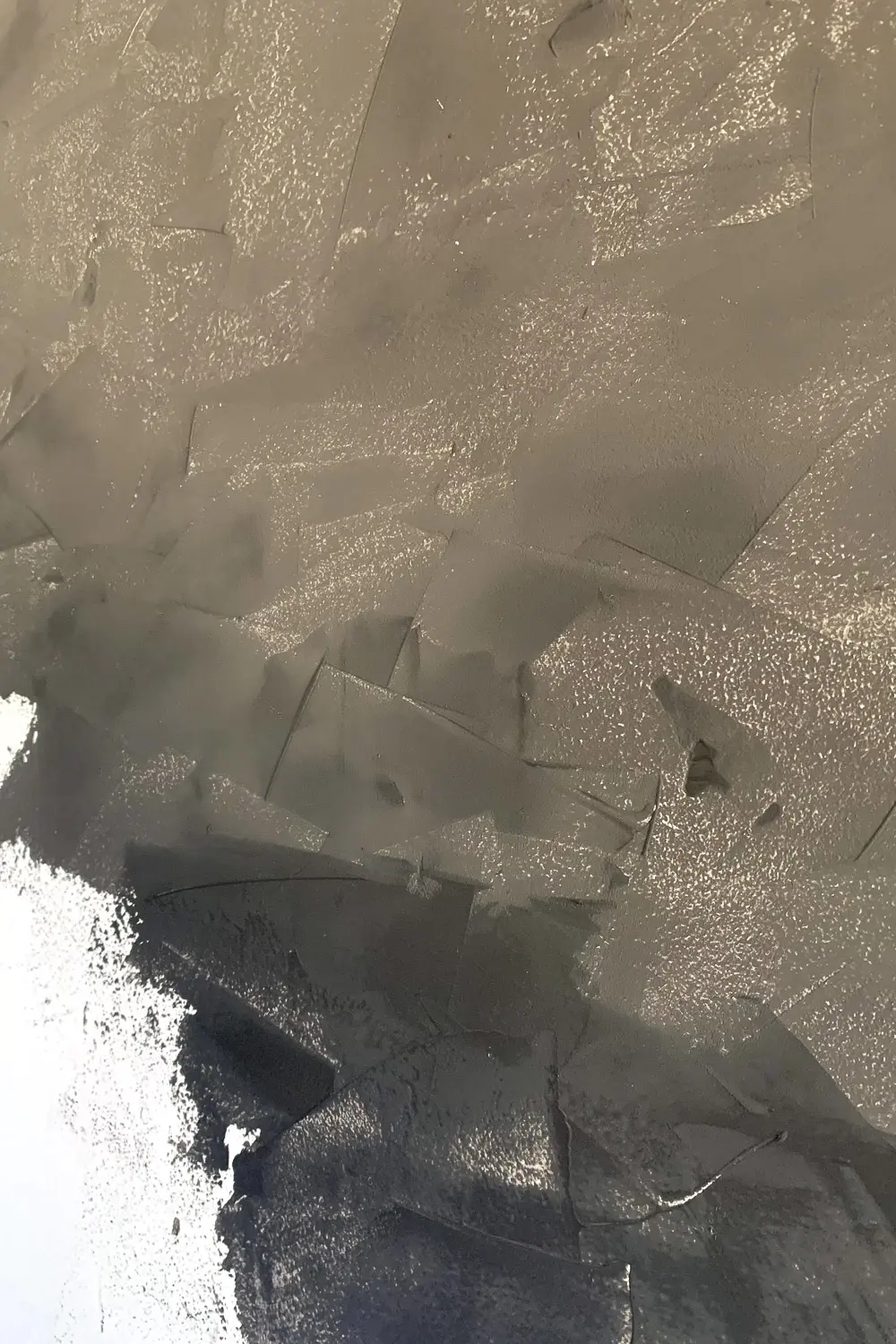 Close-up of black plaster texture showing crisscross knife strokes and natural ridges with some white primer visible at edges