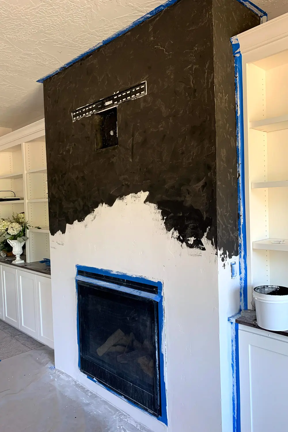 Fireplace wall with first coat of black plaster on upper section, lower section still white primer, TV mount and media box visible