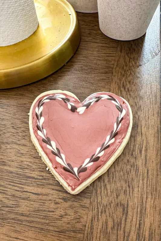 Pink Valentine heart sugar cookie decorated with royal icing without meringue powder, featuring a braided piped border in white and dark icing.