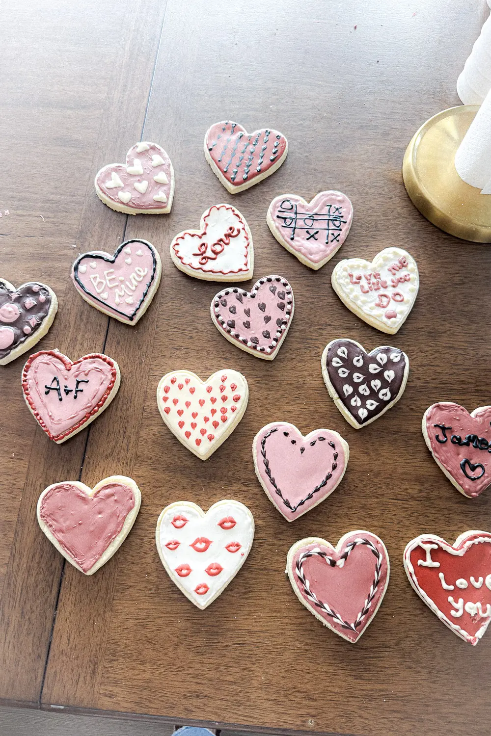 Overhead photo of Valentine heart sugar cookies decorated with royal icing without meringue powder, arranged on a wooden table with piped designs and messages.