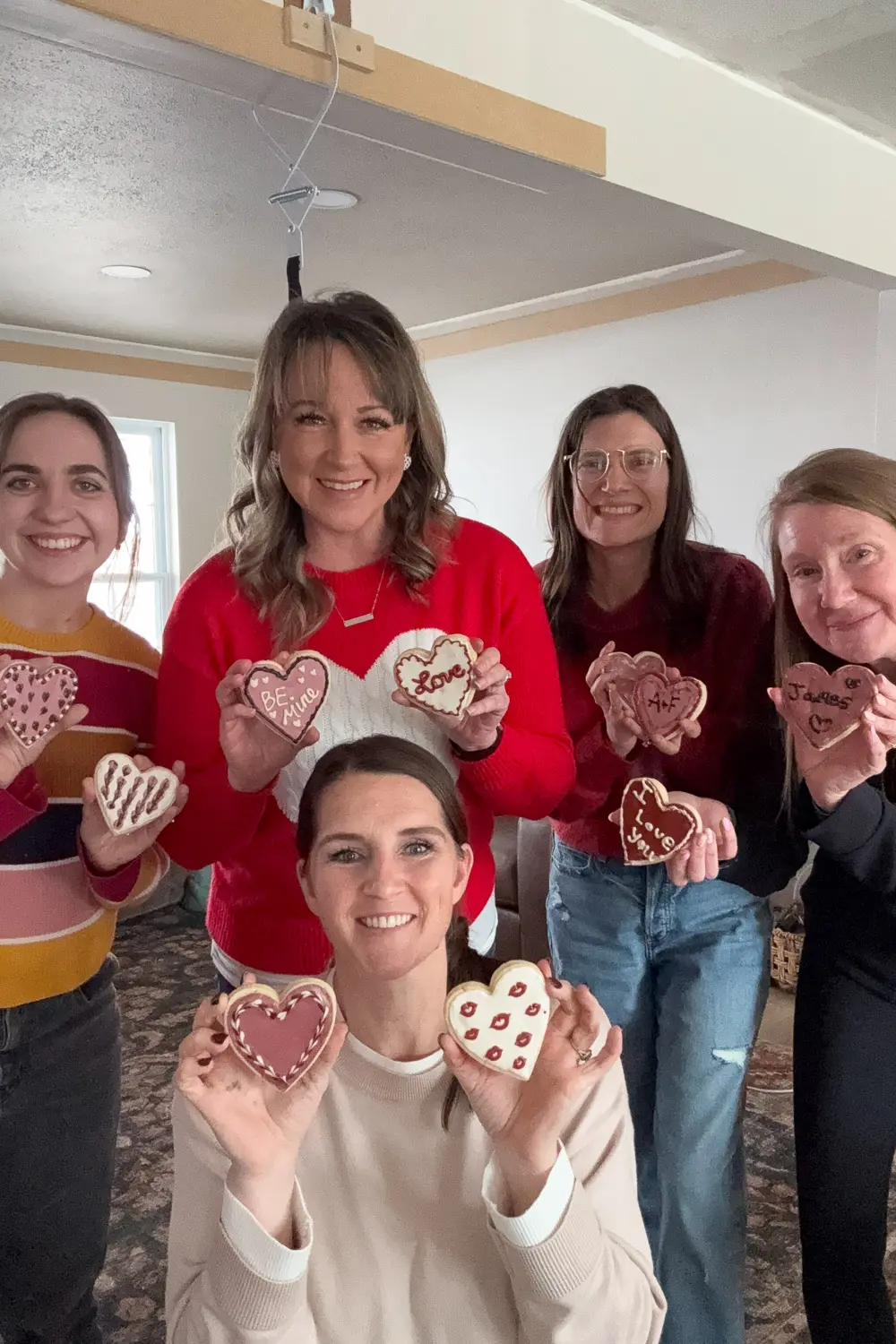 Group of women holding Valentine cookies decorated, showing finished designs like “Be Mine” and “I love you.”
