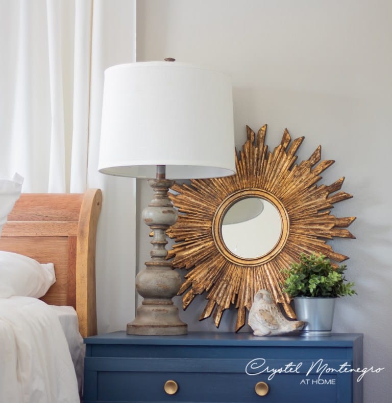 Blue nightstand with gold knobs and a lamp with gold mirror