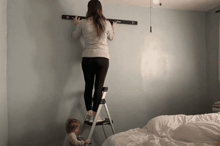 woman on ladder with level on wall