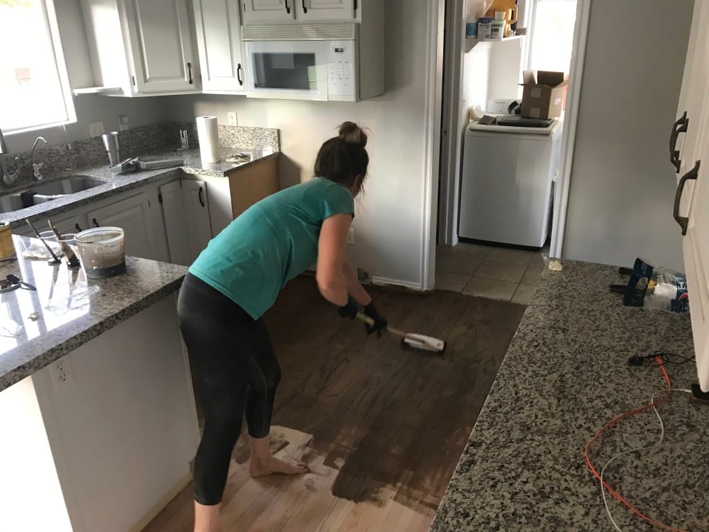 Woman staining a wood floor in a ktichen
