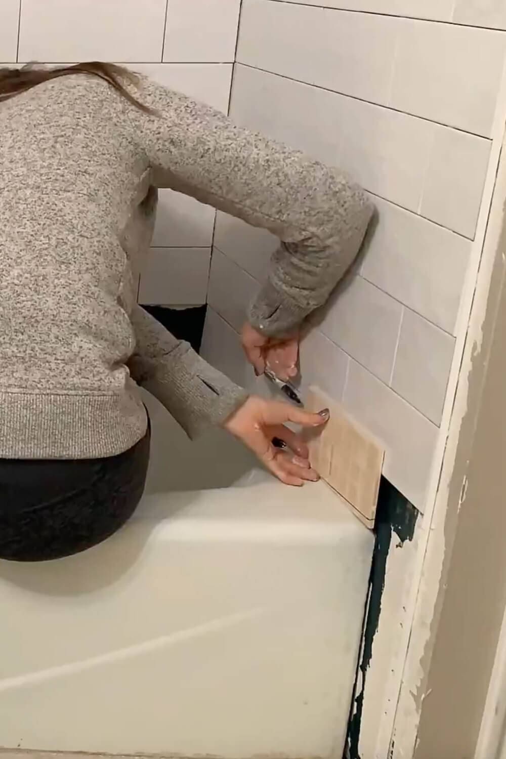 Measuring a cut tile to fit at the edge of the tub.
