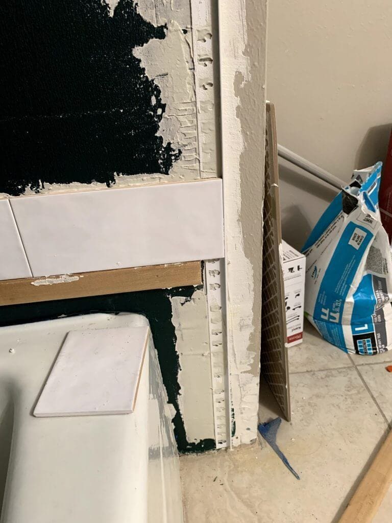 First row of white subway tiles resting on a ledger board along the shower wall.