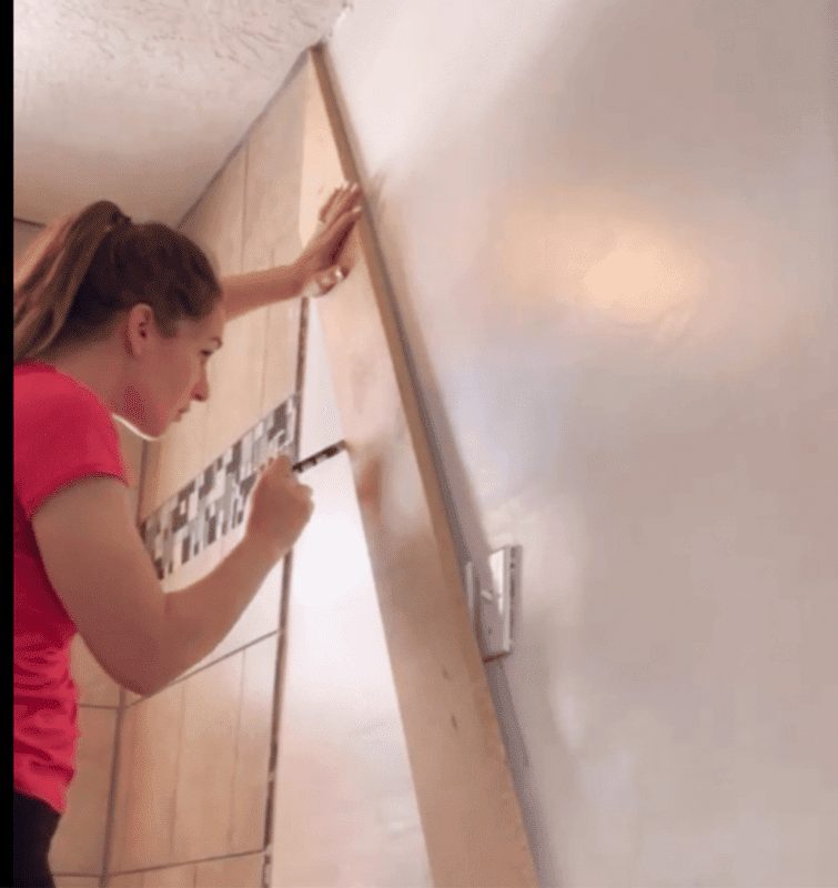 woman using wood to draw a straight line on bathroom wall