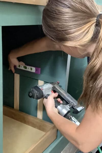 Crystel brad nailing upper drawer spacers inside a green cabinet cubby
