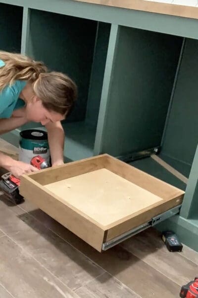Crystel setting a pine drawer onto its slides inside a green cabinet
