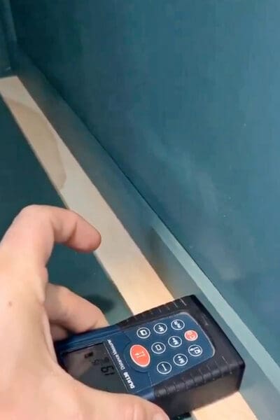laser measure held against a pine spacer to measure the width for a drawer with slides