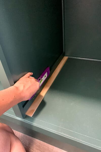 checking a drawer spacer with a small level before brad nailing it to the cabinet wall