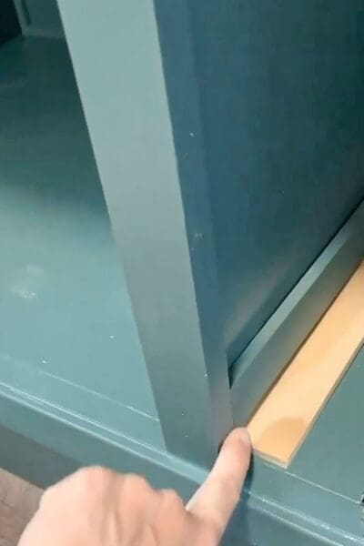 finger pointing at the face frame lip next to a pine drawer spacer inside a green cabinet