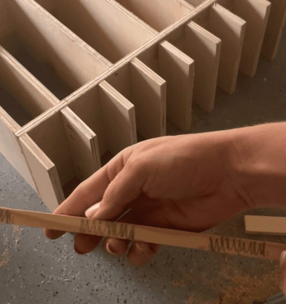 A woman holding wood that is helping her build a tool organizer