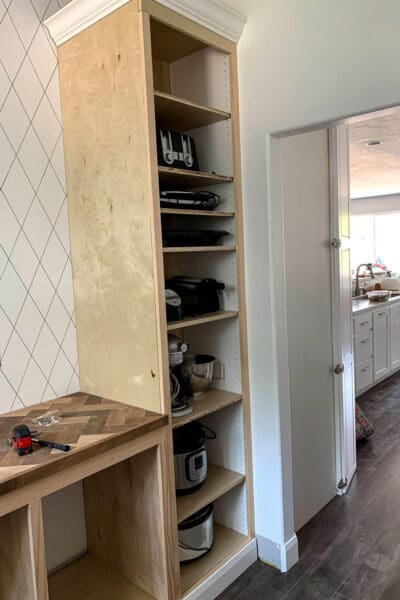 small appliances test fit on unpainted plywood shelves in a DIY butler's pantry cabinet