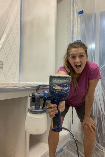 Crystel holding a HomeRight paint sprayer in the half painted pantry