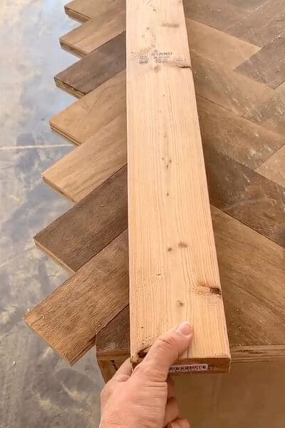 hand holding a straight 2x4 across the herringbone boards to check the cut line