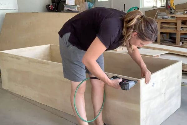 Crystel brad nailing a plywood base cabinet together in the garage