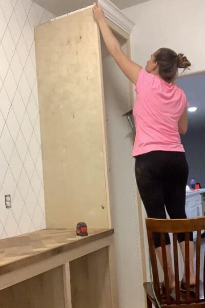 Crystel on a chair adding crown molding to the tall pantry cabinet