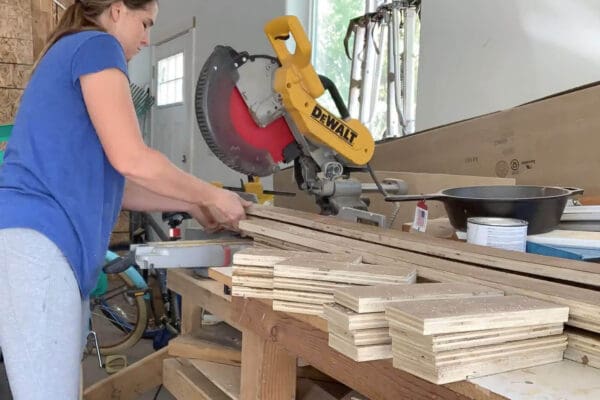 Crystel cutting 8 inch herringbone boards on a miter saw next to a stack of finished boards