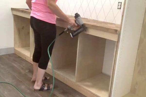 Crystel nailing a pine face frame onto the cubby cabinet with a brad nailer