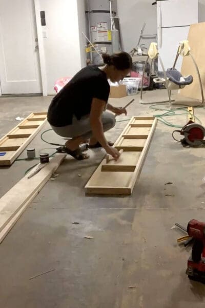Crystel nailing the plywood top to a DIY floating shelf frame in the garage