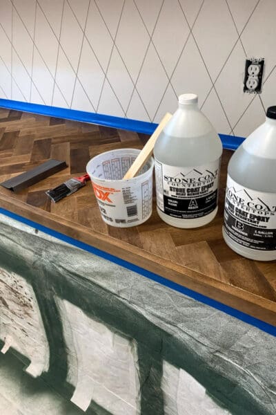 Stone Coat epoxy bottles and a mixing bucket on a taped off herringbone countertop