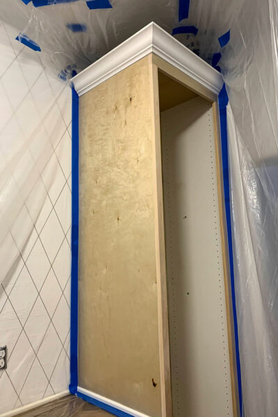 tall pantry cabinet taped off with plastic and painter's tape for spray paint