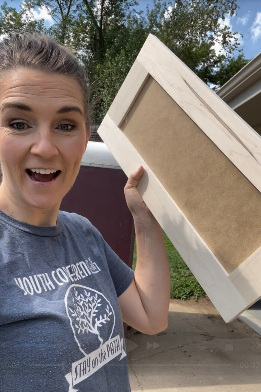 Person holding a custom unfinished cabinet door, excited about progress in an affordable kitchen remodel.