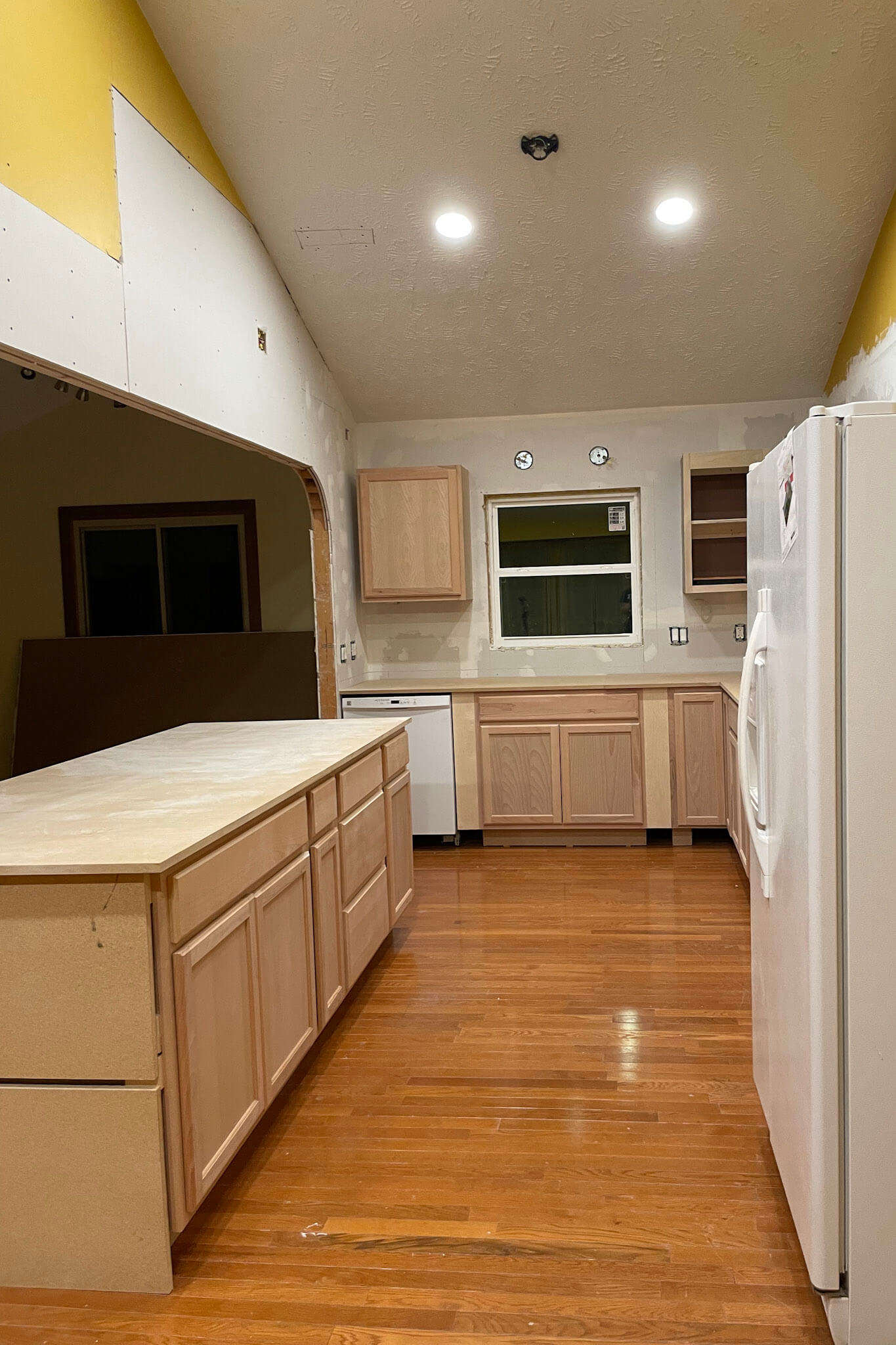 Kitchen in progress during an affordable kitchen remodel, featuring unfinished wood cabinets, a large island, and hardwood floors.