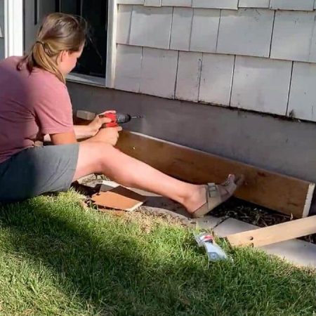 woman drilling into concrete on house