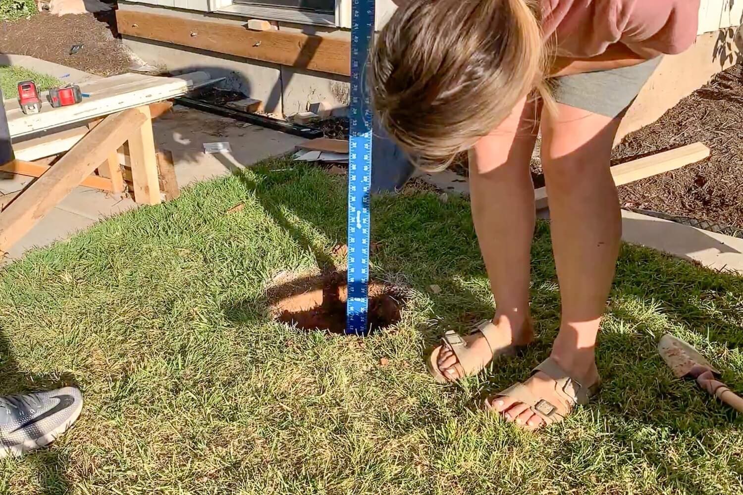 Measuring the post hole depth to confirm it reached 18 inches deep.
